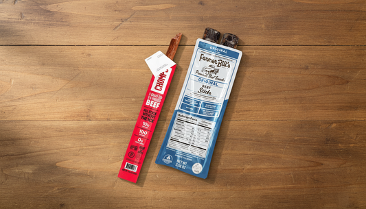 Chomps and Farmer Bill's beef stick packages laid side by side on a wood table, overhead size comparison