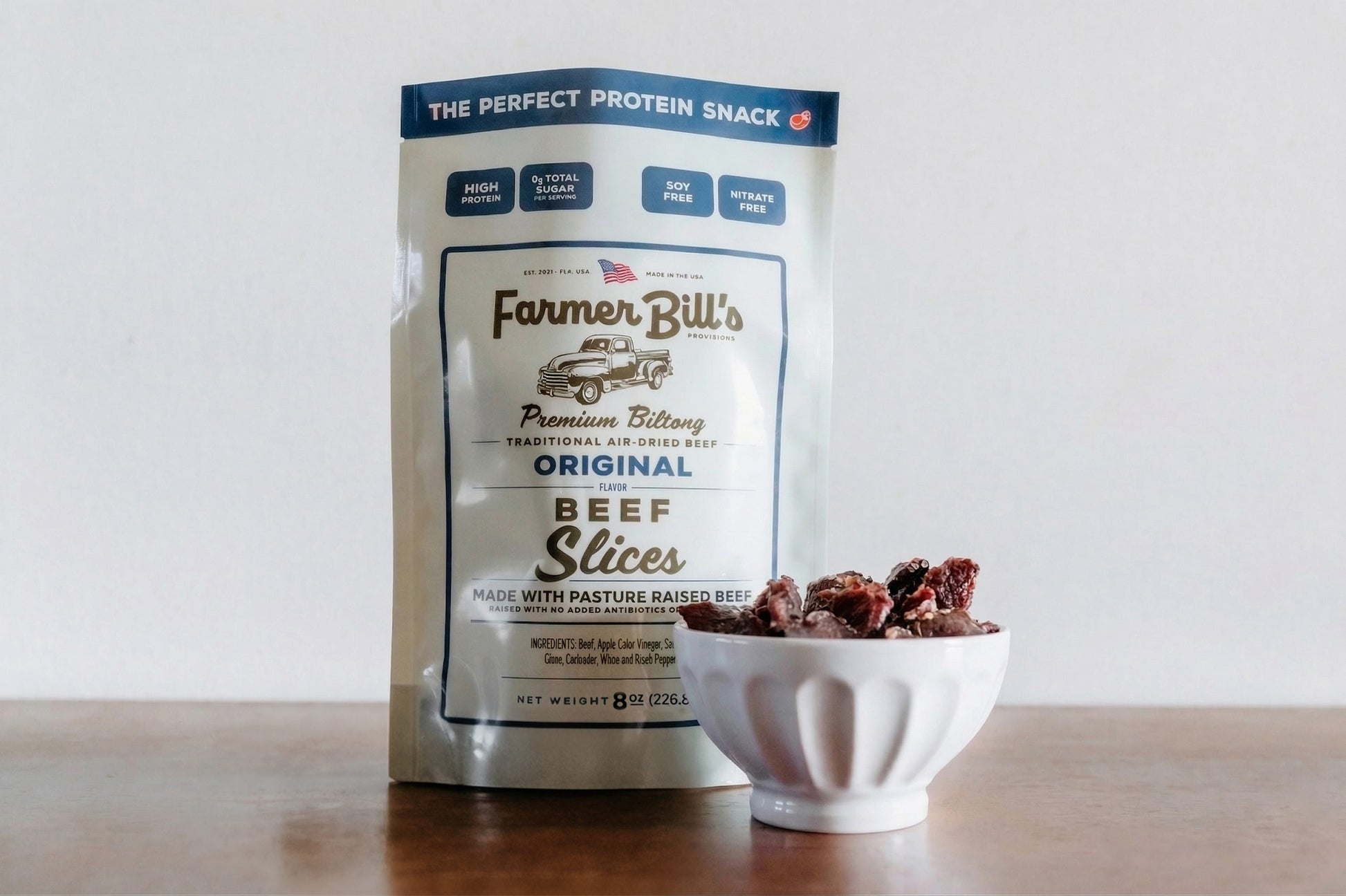 Farmer Bill's Original beef biltong slices in white bowl next to package front.